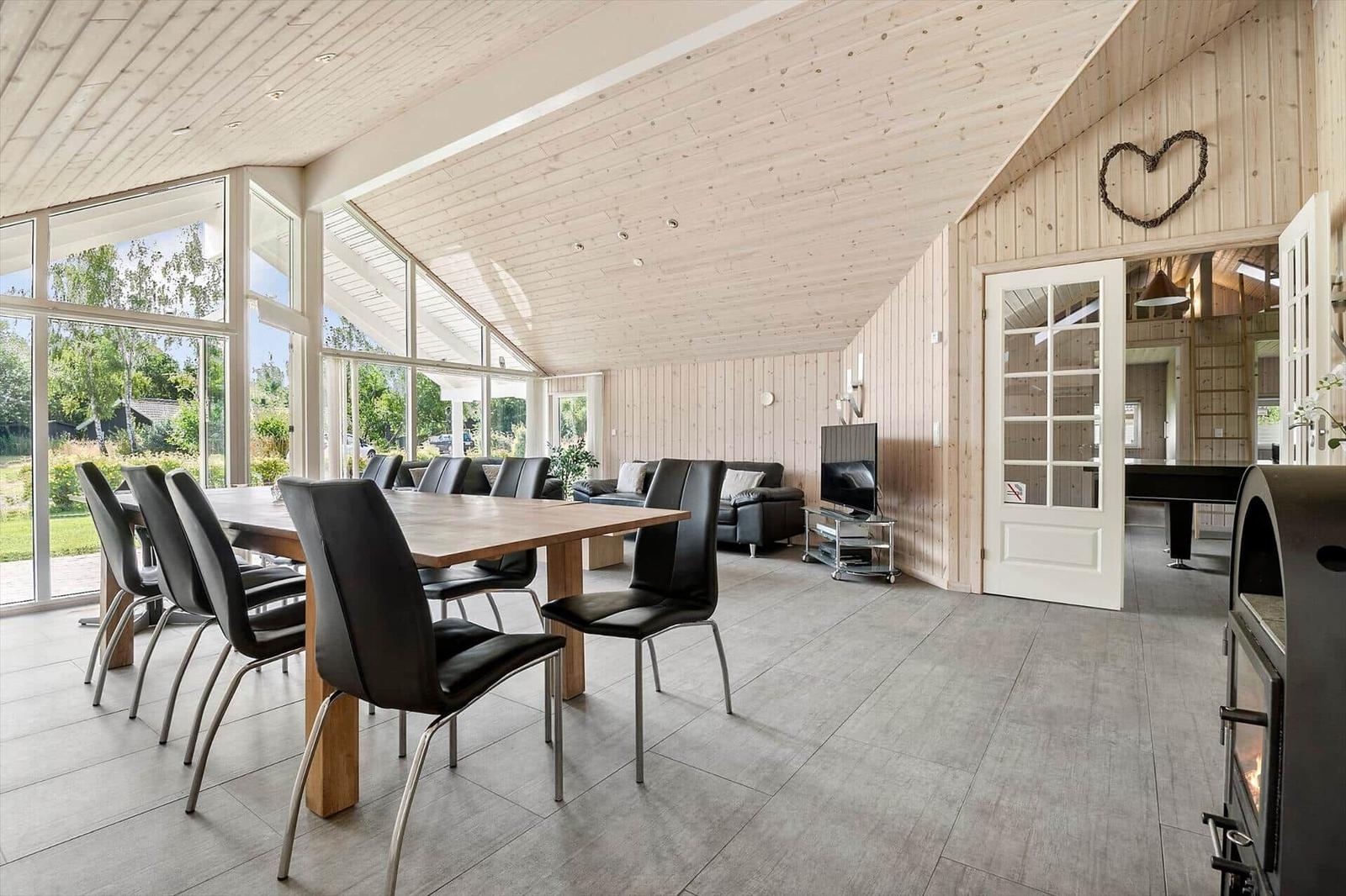 Large room with dining table, sofa, and TV. Wooden walls, large windows, and fireplace.