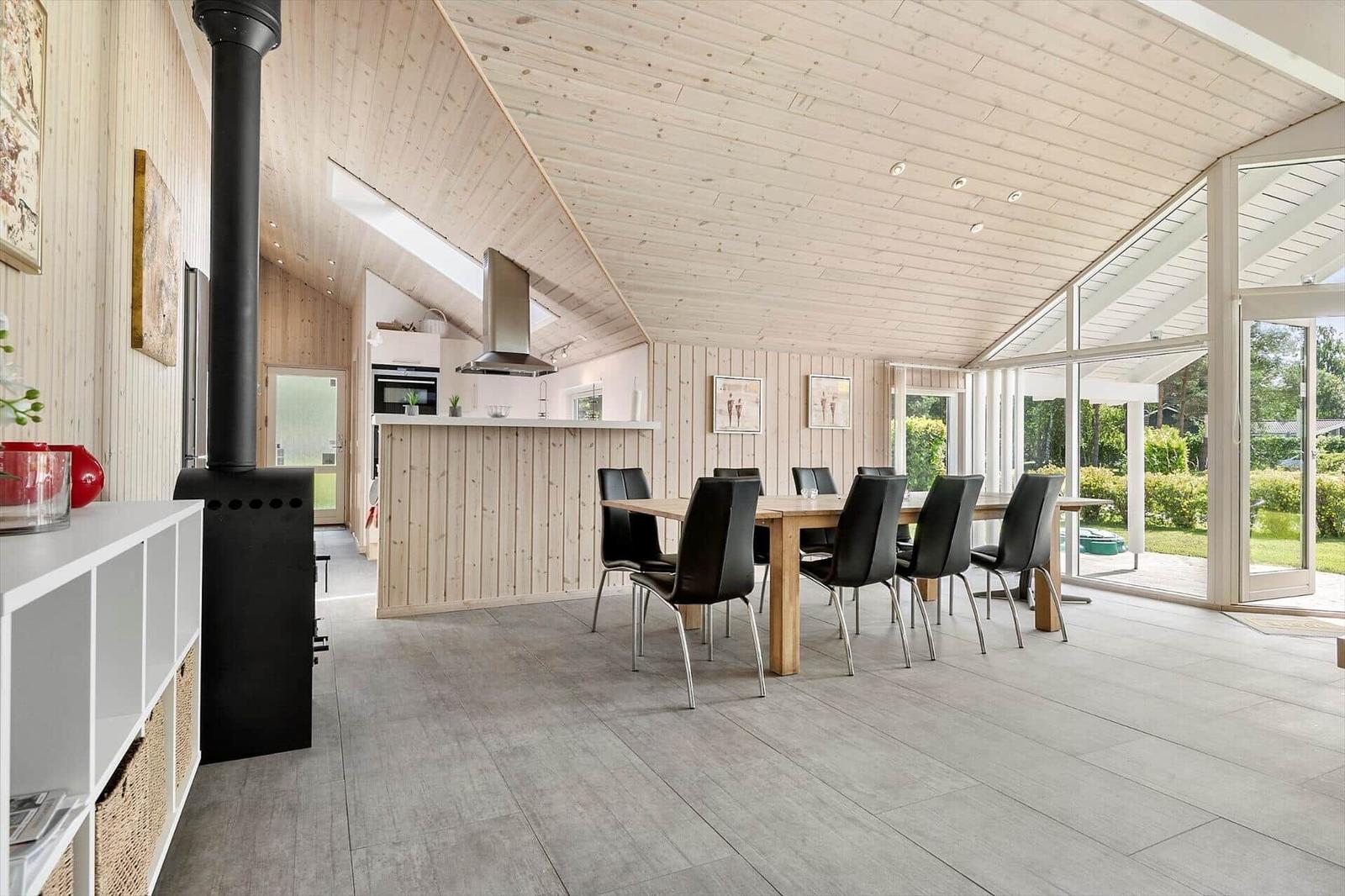 Large dining area with wooden table and chairs, kitchen, and terrace with glass doors.