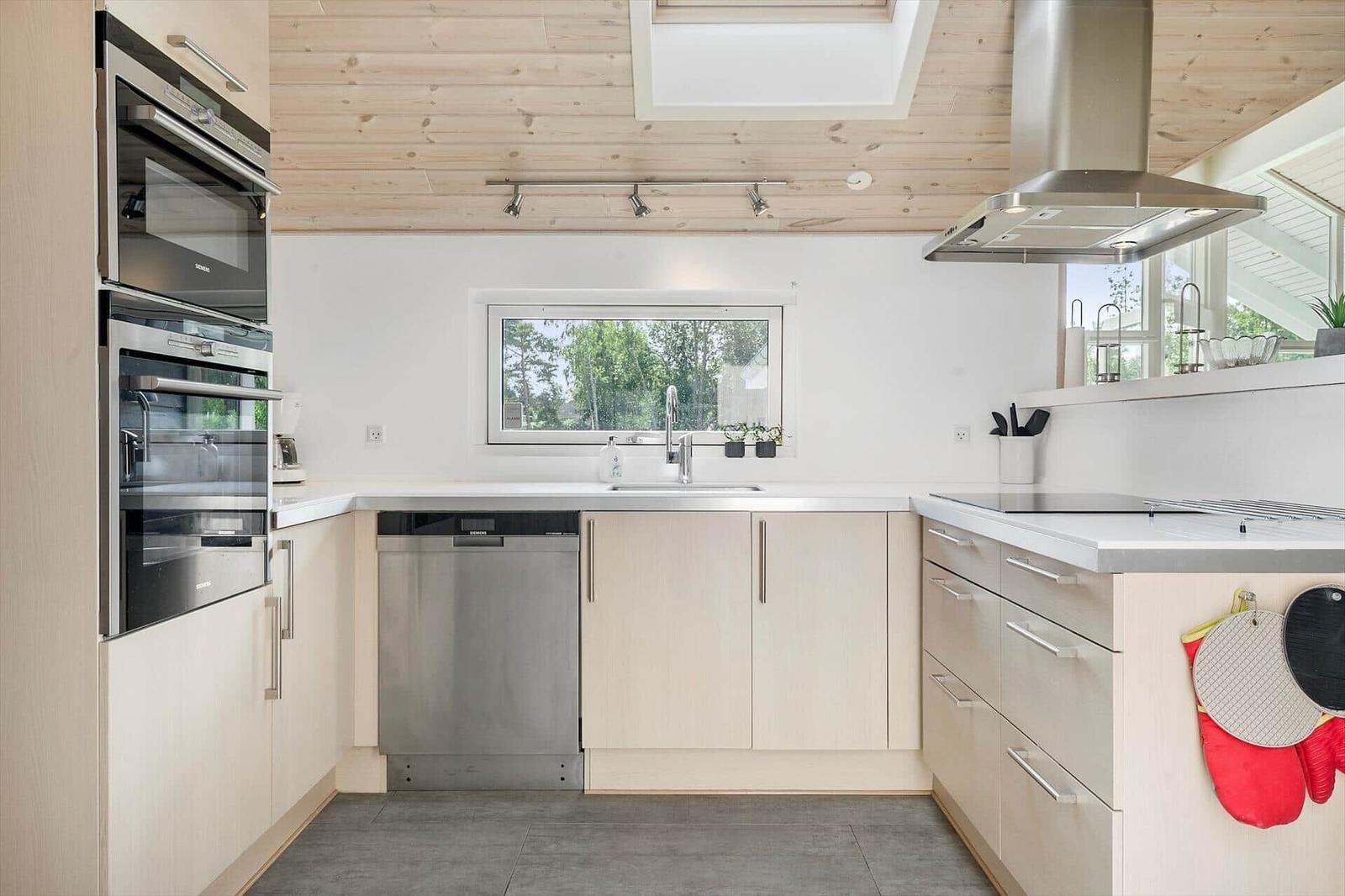 Modern kitchen with stainless steel appliances, wooden ceiling, and window view.