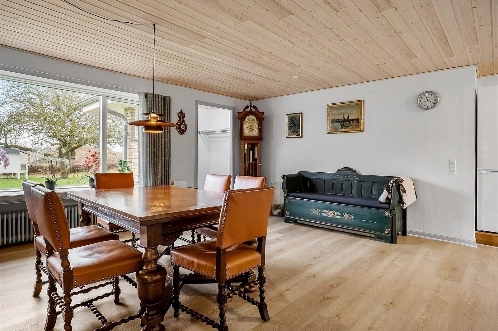 Esszimmer mit Holztisch, Lederstühlen und grüner Bank. Holzdecke und große Fenster.