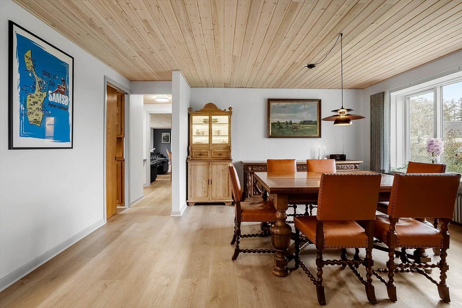 Esszimmer mit Holztisch, Lederstühlen und Wandbildern. Holzdecke und Boden.