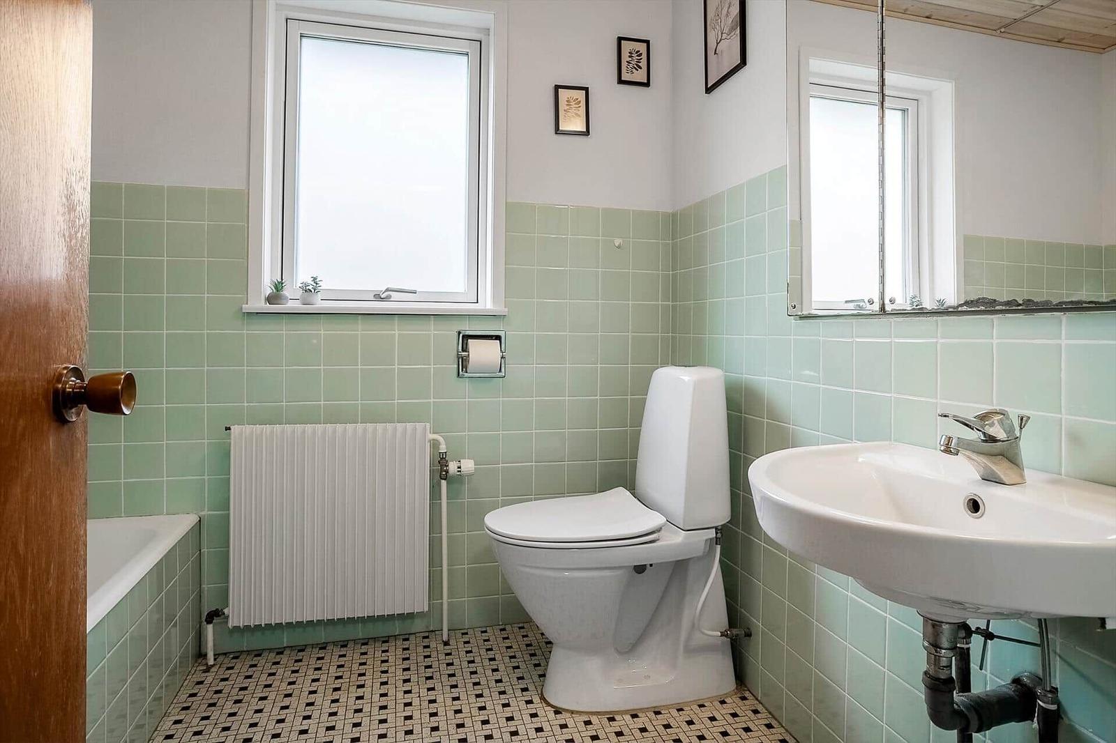 Badezimmer mit Toilette, Waschbecken und Fenster. Wandfliesen und Mosaikboden.