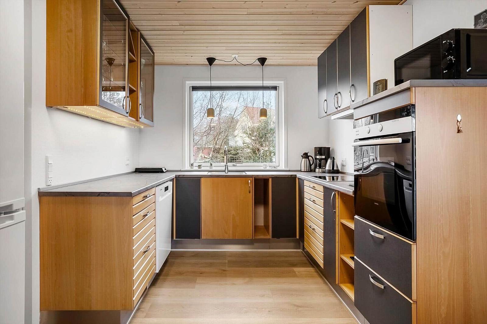 Küche mit Holz- und Schrankfronten, Fenster, Spüle und Einbauküchengeräten.