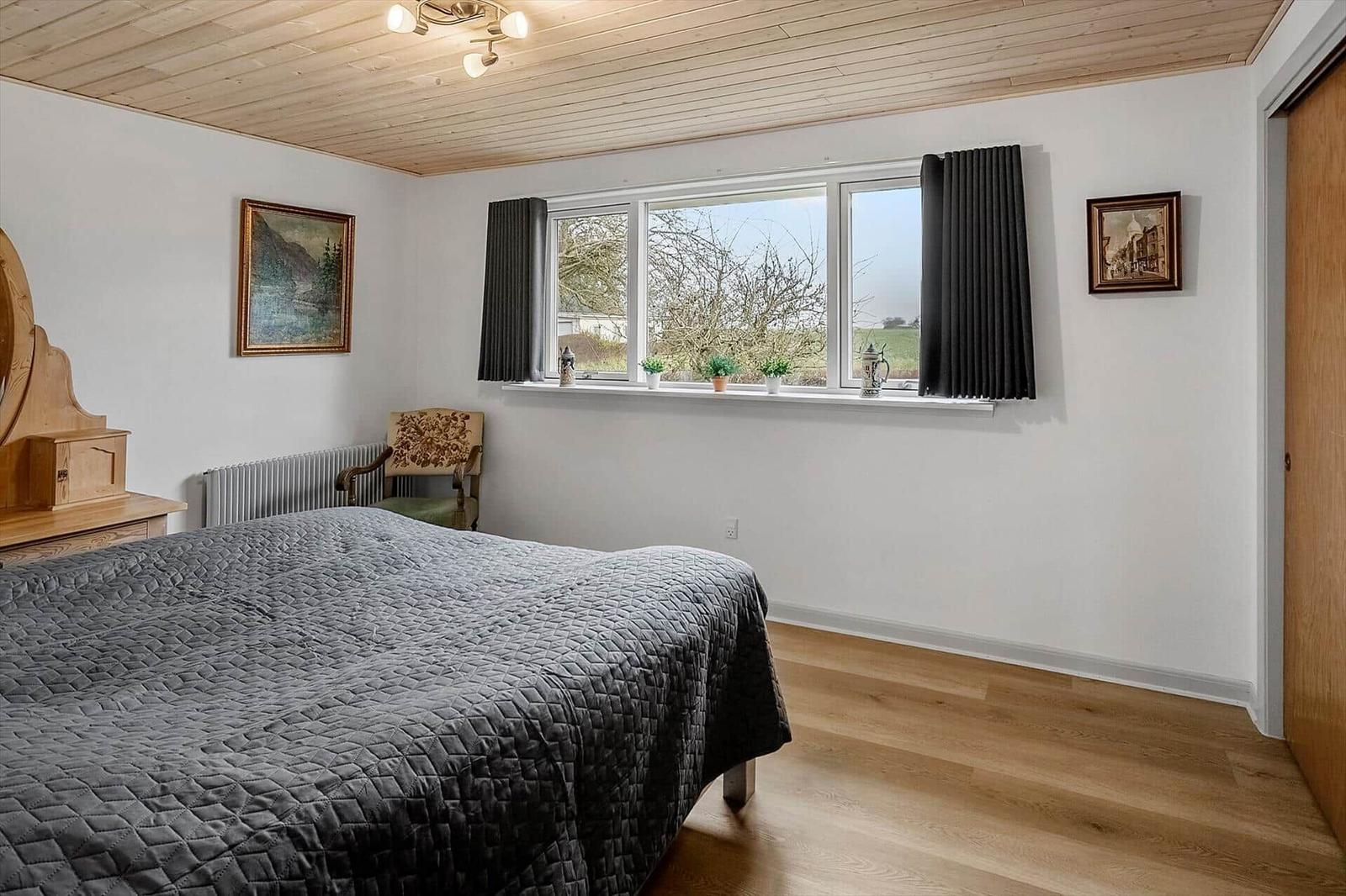 Schlafzimmer mit Bett, Fenster und Holzboden. An der Wand hängen Bilder.
