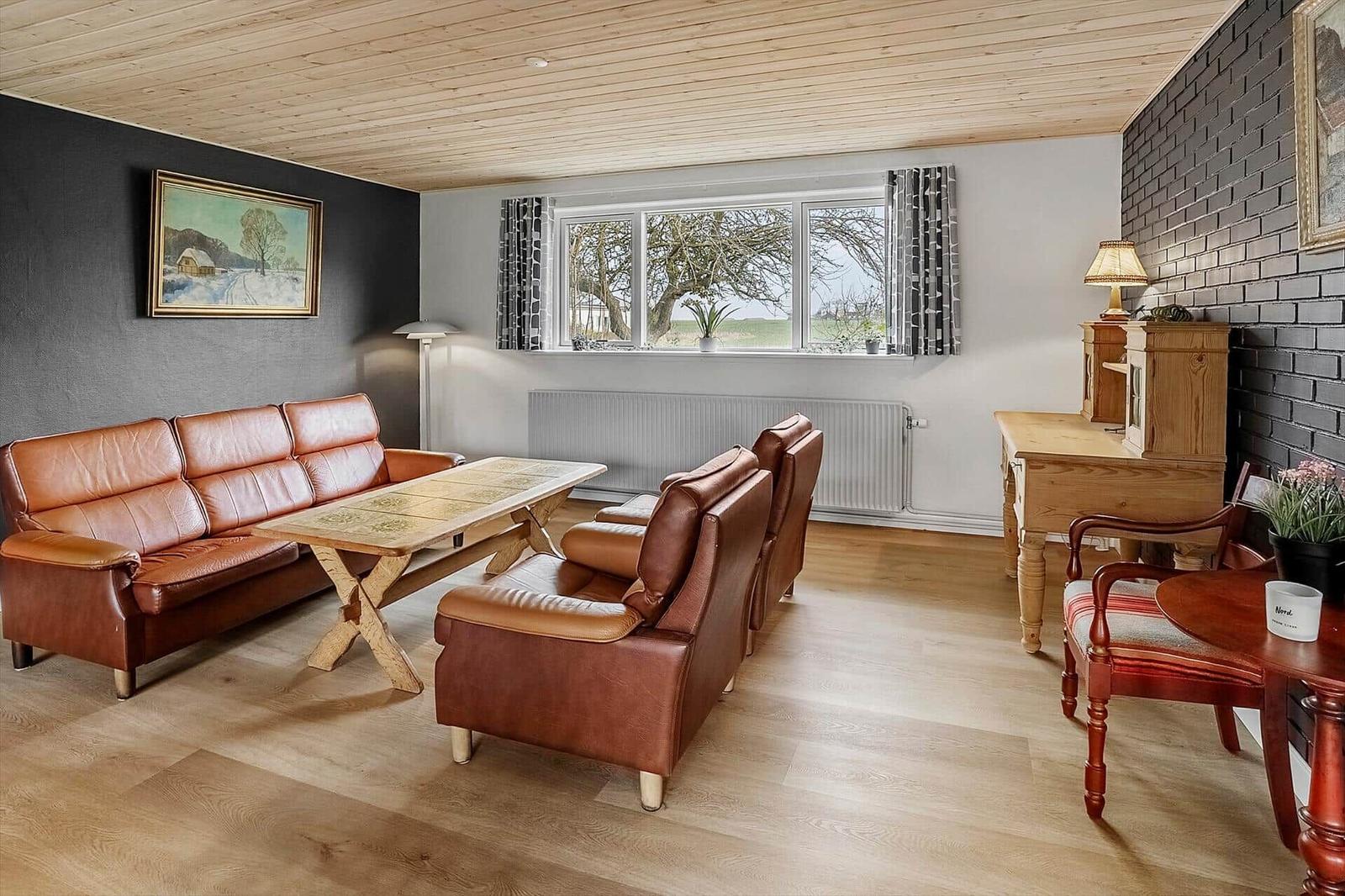Wohnzimmer mit Ledersofa, Holztisch und Blick auf Felder.