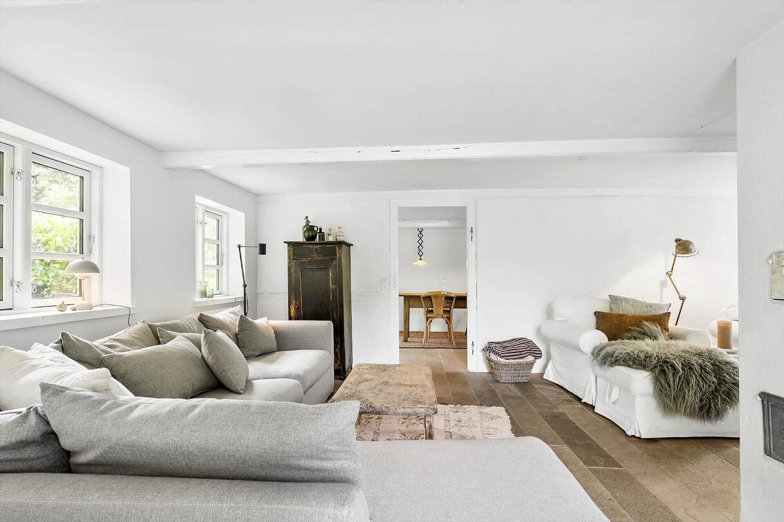 Wohnzimmer mit Sofa, Sessel und Holzboden. Durchgang zur Küche sichtbar.