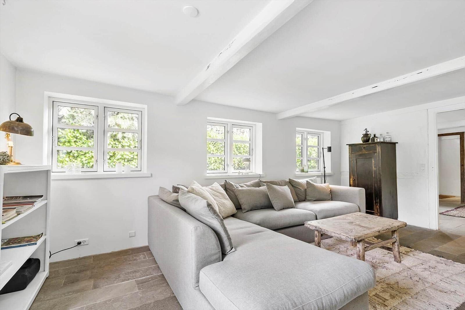Wohnzimmer mit grauem Sofa, Holztisch und Fenstern mit Blick auf Grün.