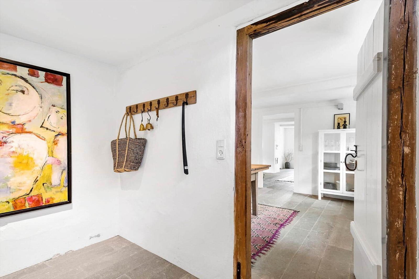 Eingangsbereich mit Wandbild und Haken für Taschen. Durchgang zu Küche mit Glasvitrine.