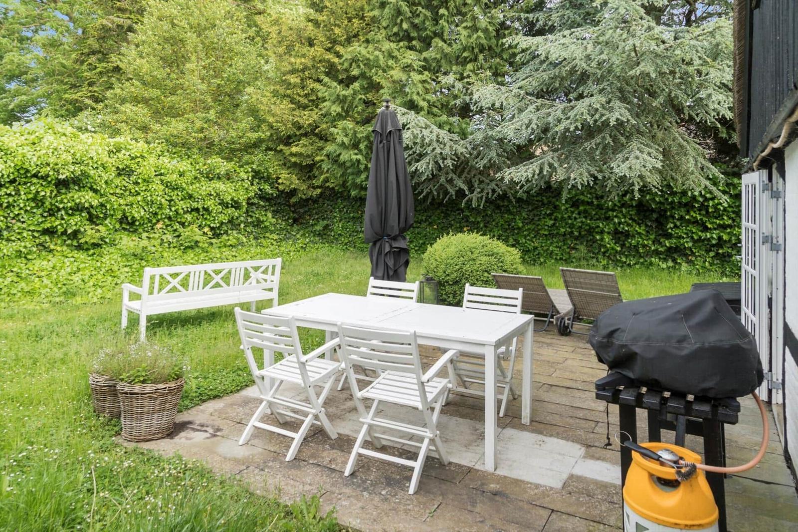 Hinterhof mit weißem Tisch, Stühlen, Bank, Grill und Sonnenliegen.