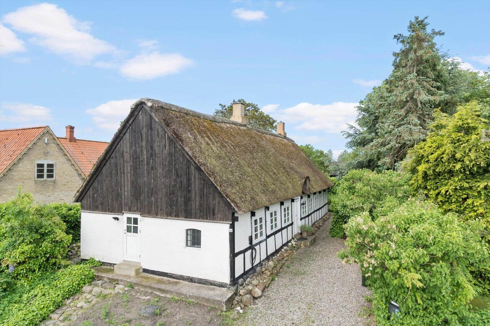 Ein traditionelles Haus mit Strohdach und Fachwerk, umgeben von Grünflächen und Bäumen.