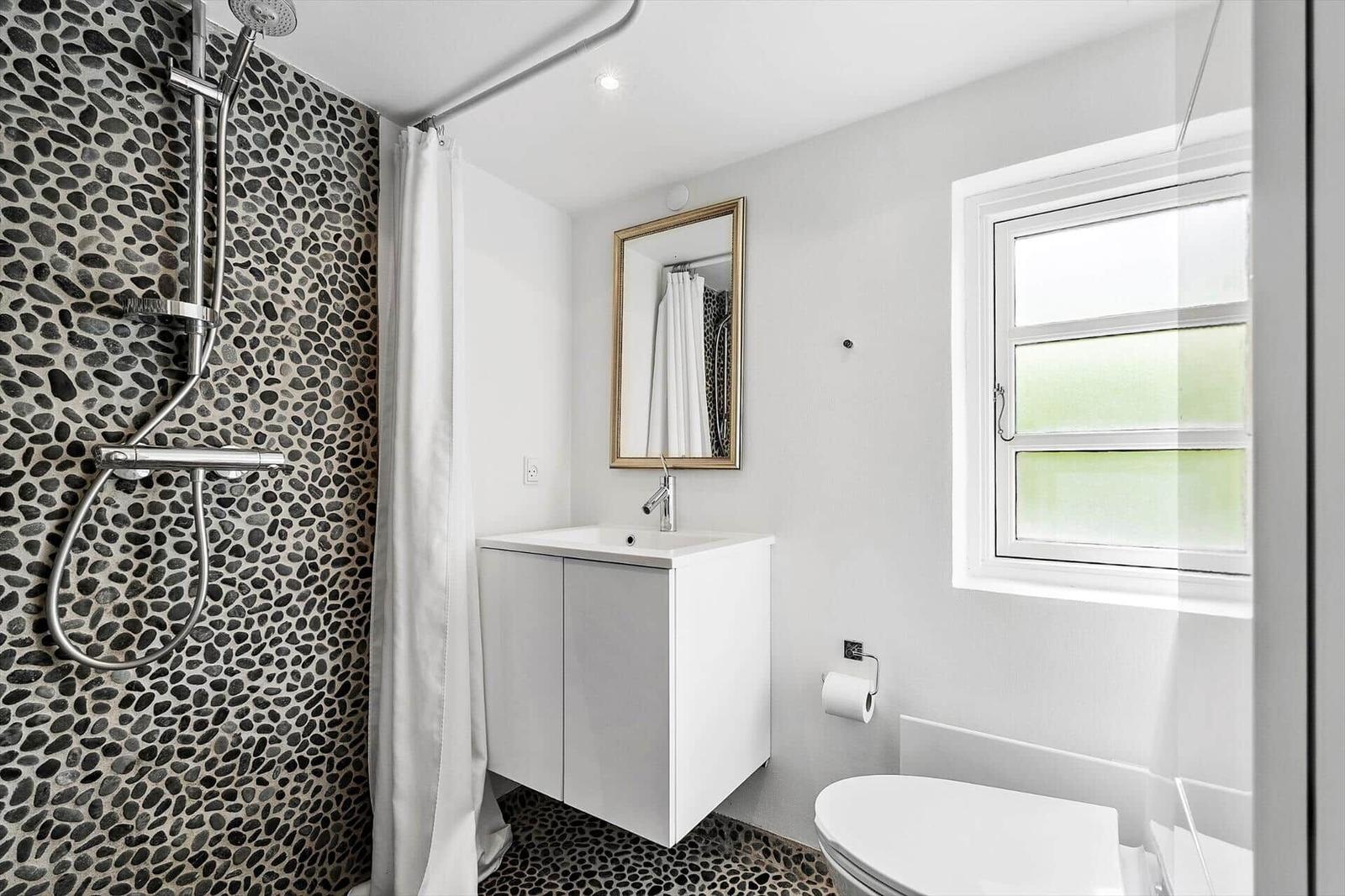 Badezimmer mit Dusche, Waschbecken und Toilette. Wände und Boden sind mit Stein verkleidet.