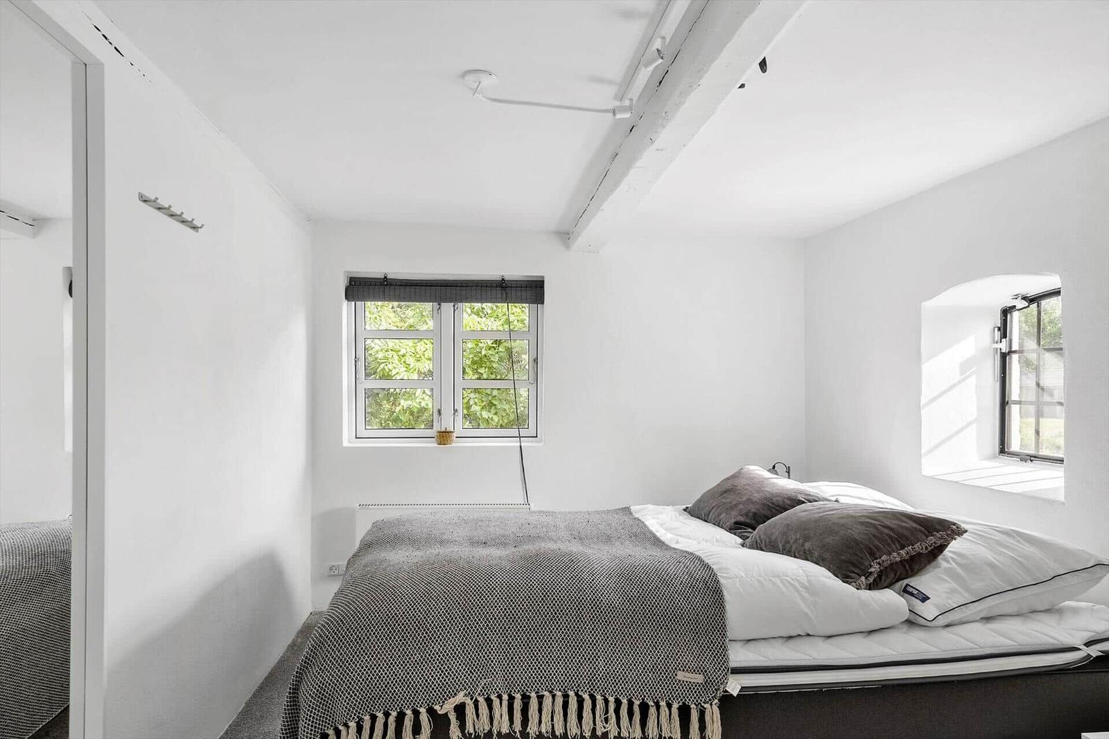 Schlafzimmer mit Bett, zwei Fenstern und weißen Wänden.