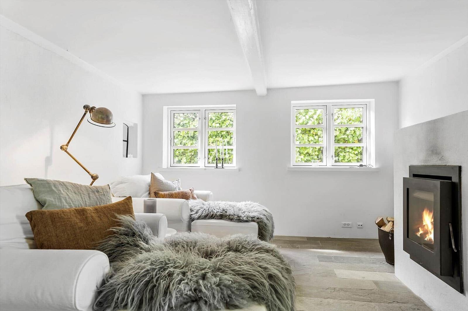 Wohnzimmer mit Sofa, Kamin und zwei Fenstern. Holzboden und weiße Wände.