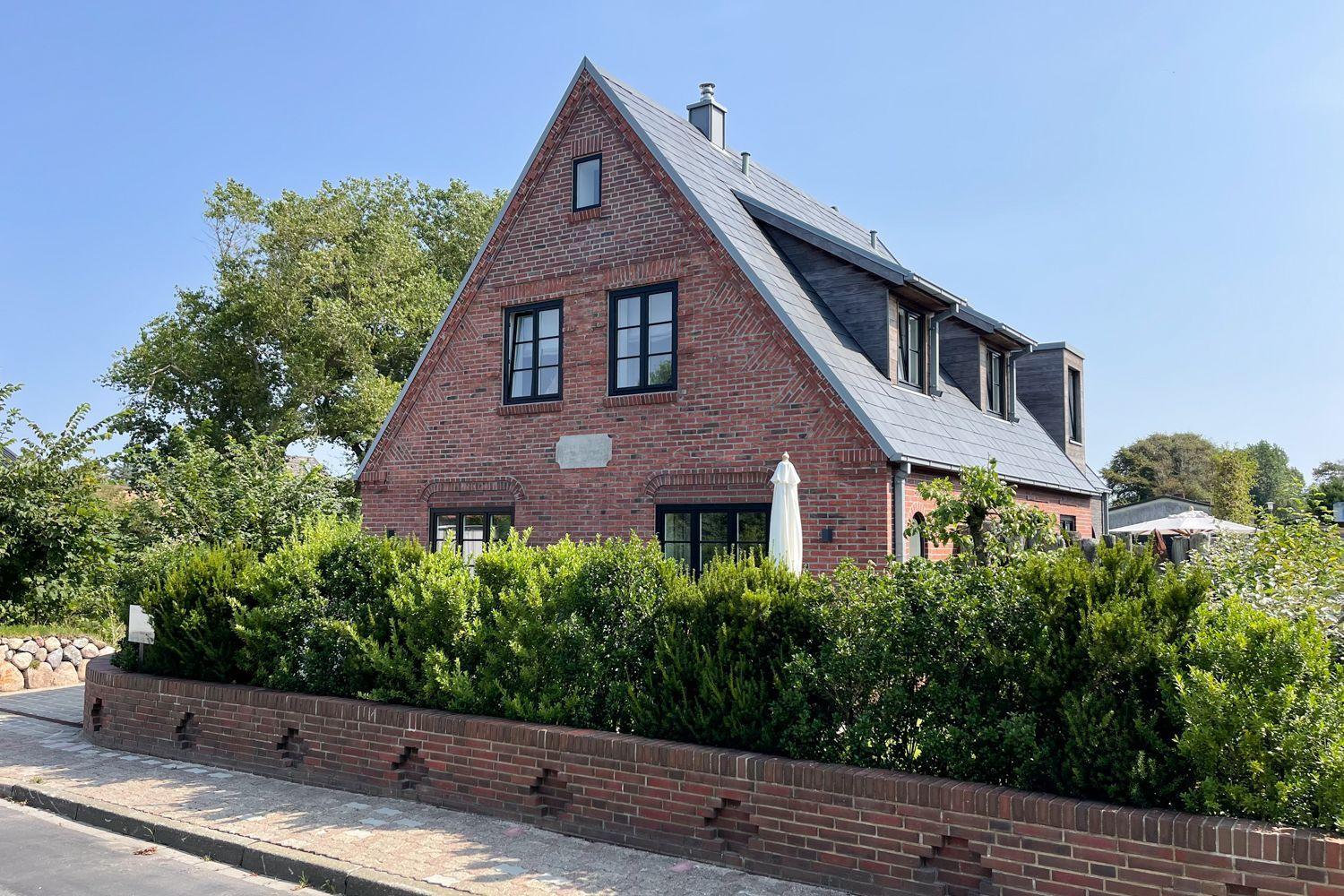 Rotes Backsteinhaus mit Dachgauben und grüner Hecke im Vorgarten.