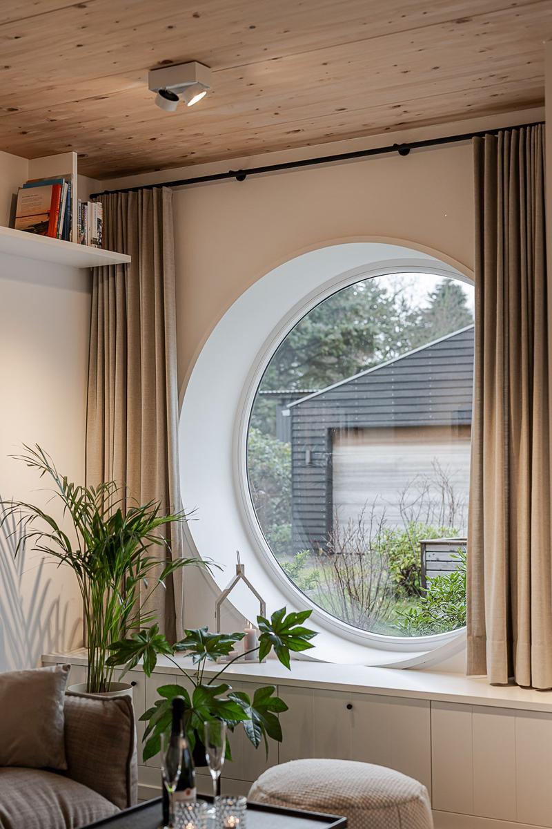 Rundes Fenster mit Vorhängen, Pflanzen und Sitzgelegenheit im Wohnbereich.