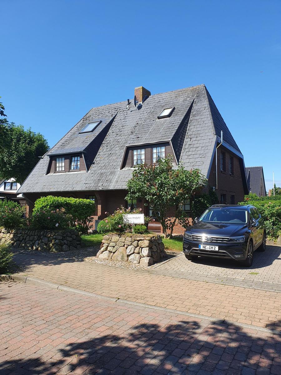 Haus mit schwarzem Dach, Steinmauer und gepflastertem Hof. Ein Auto steht vor dem Eingang.