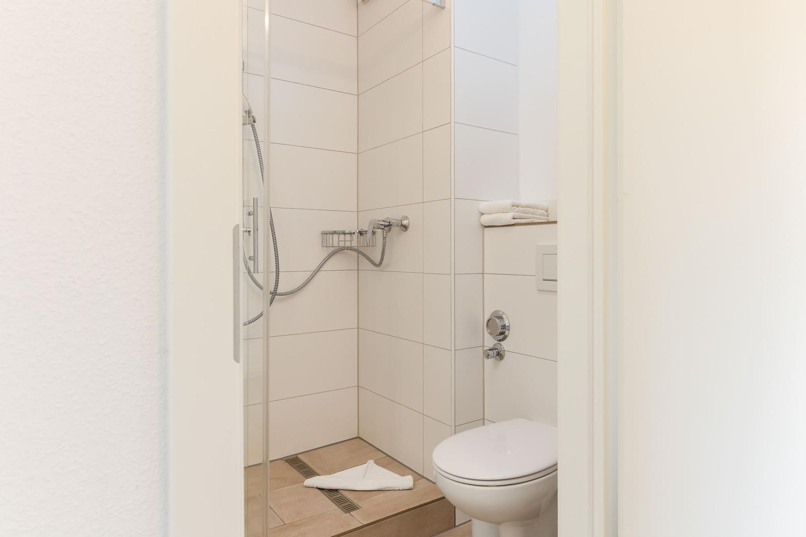 Dusche mit Duschbrause und Toilette in weißer Fliesenwand