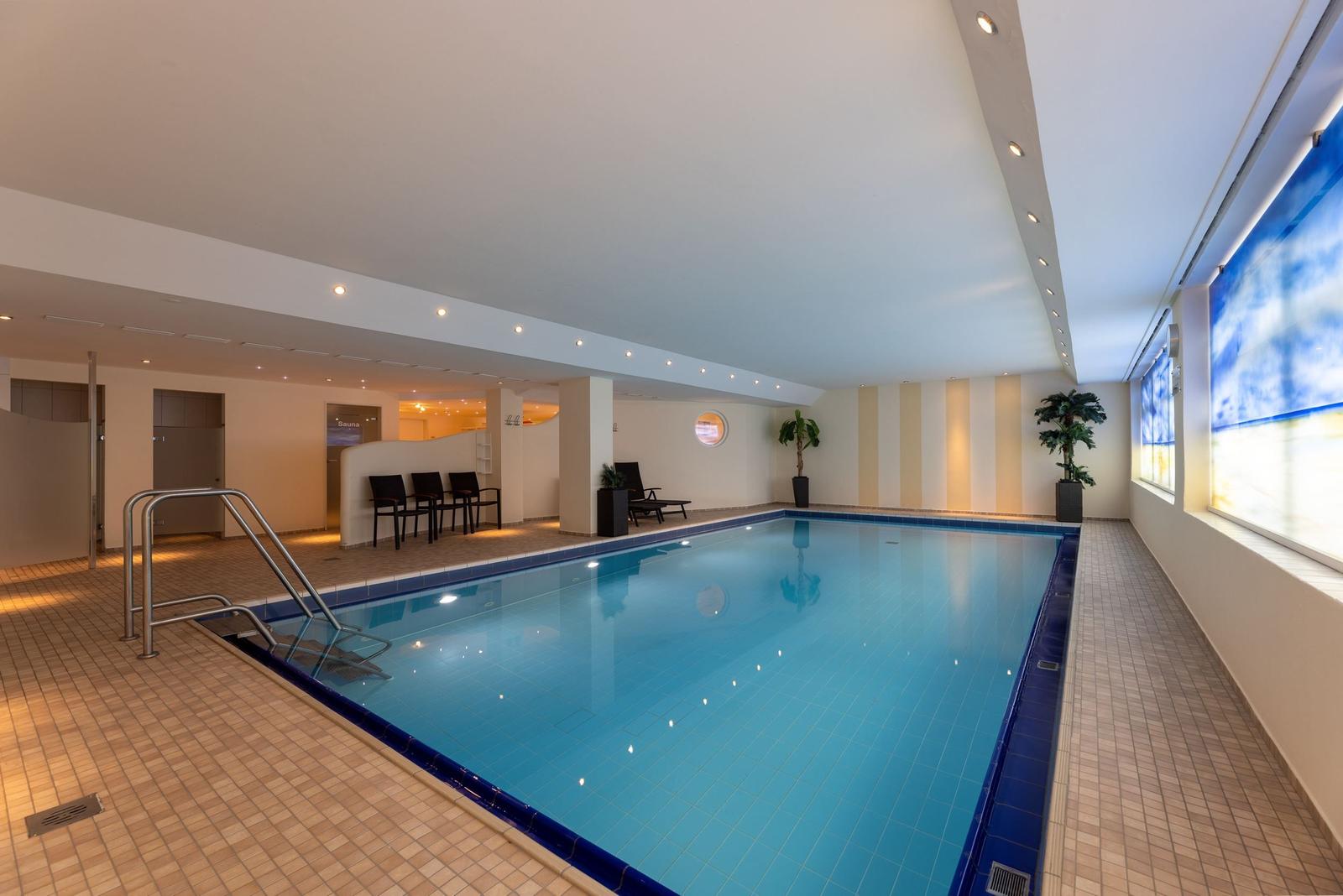 Innenpool mit Sauna, Liegestühlen und Pflanzen an den Wänden.