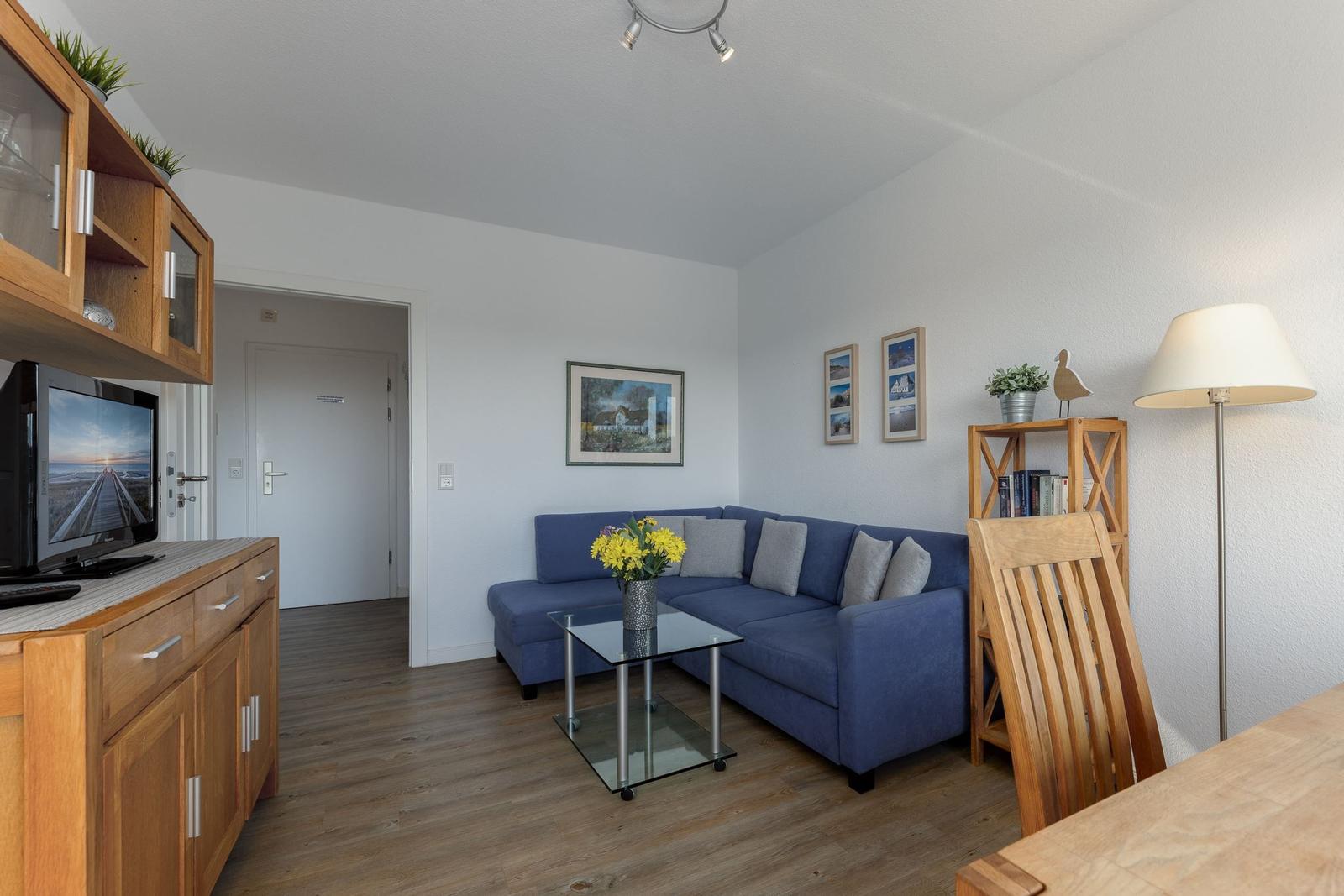 Wohnbereich mit blauem Sofa, Glas-Tisch und Holzmöbeln.