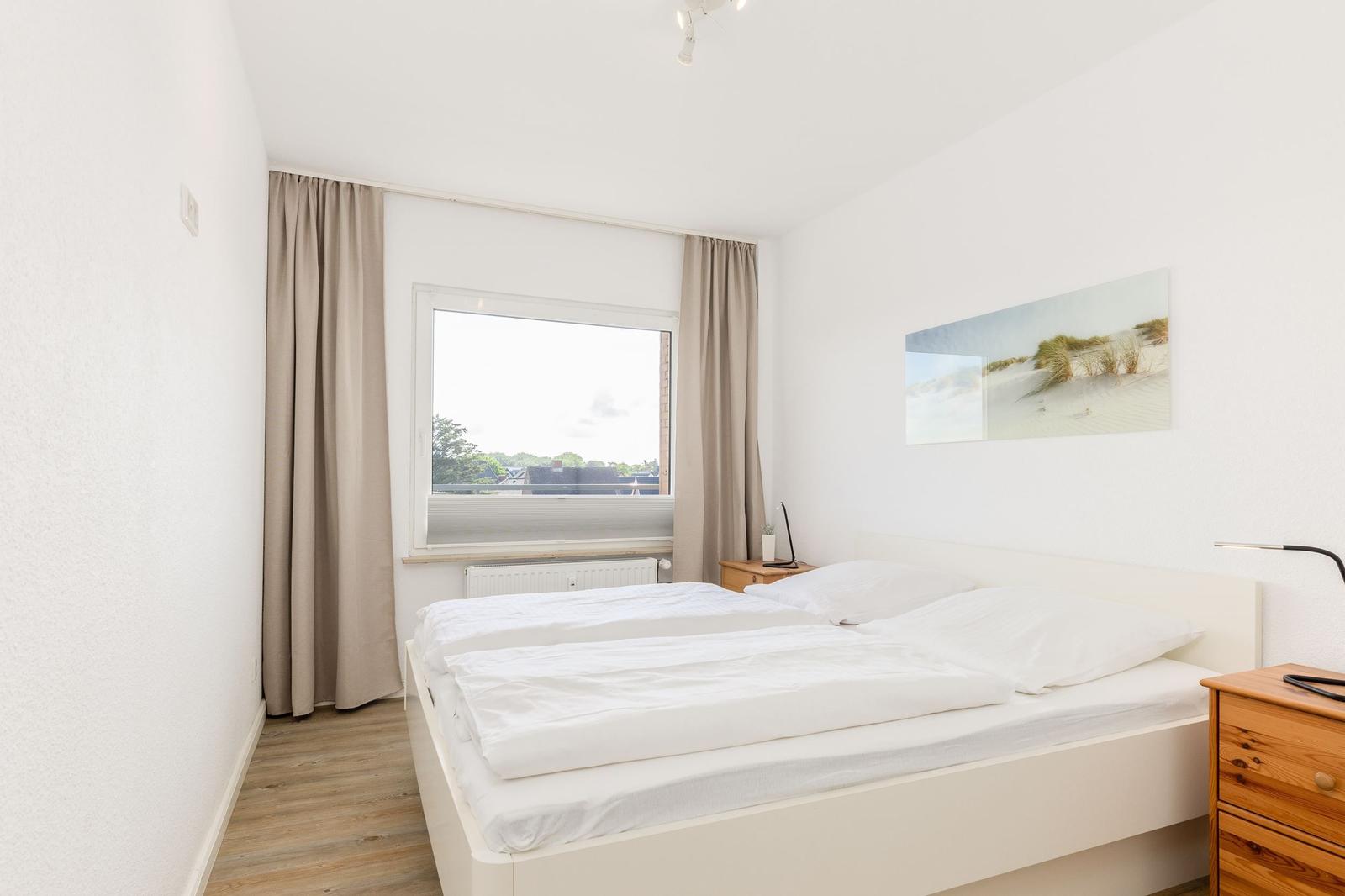 Schlafzimmer mit weißem Bett, Holzschrank und Fenster mit Blick.