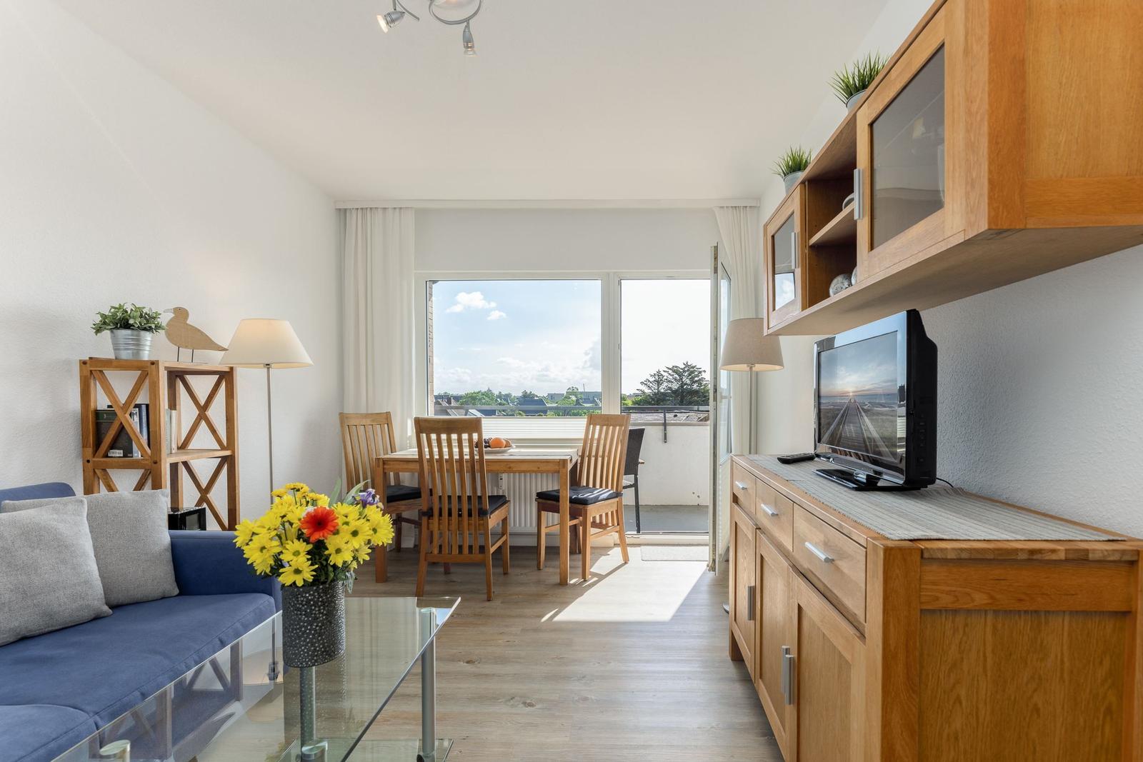 Wohnzimmer mit Essbereich, Balkon und Holzmöbel. Fernseher auf Schrank.