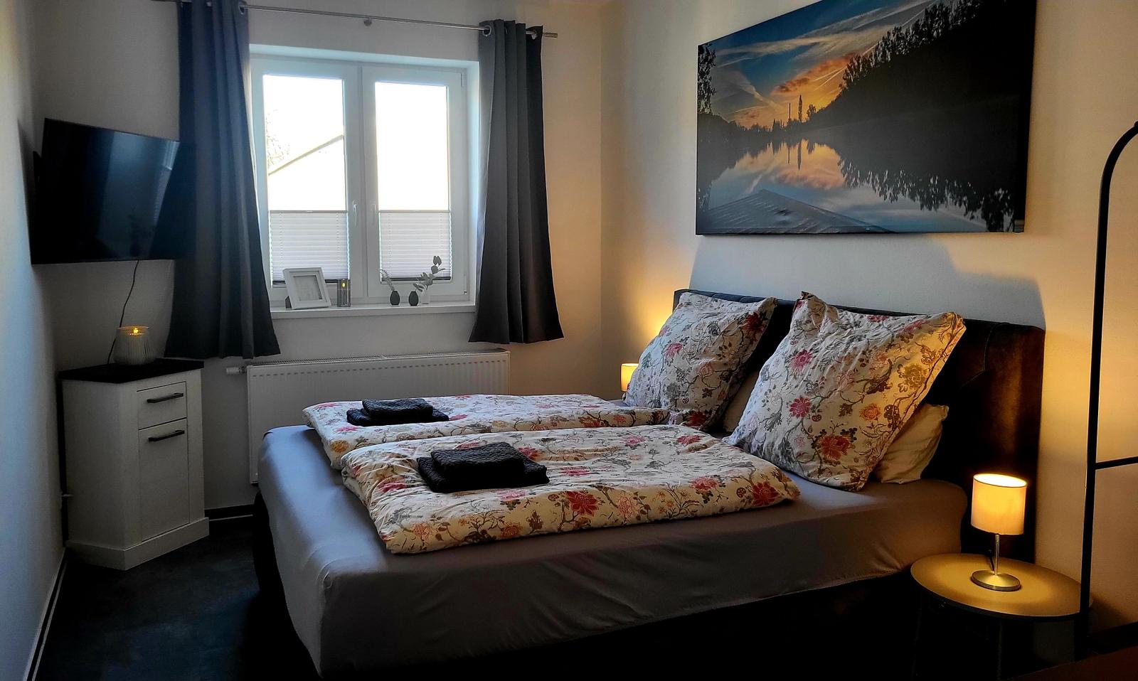 Schlafzimmer mit Bett, Fenster, Fernseher und Wandbild.