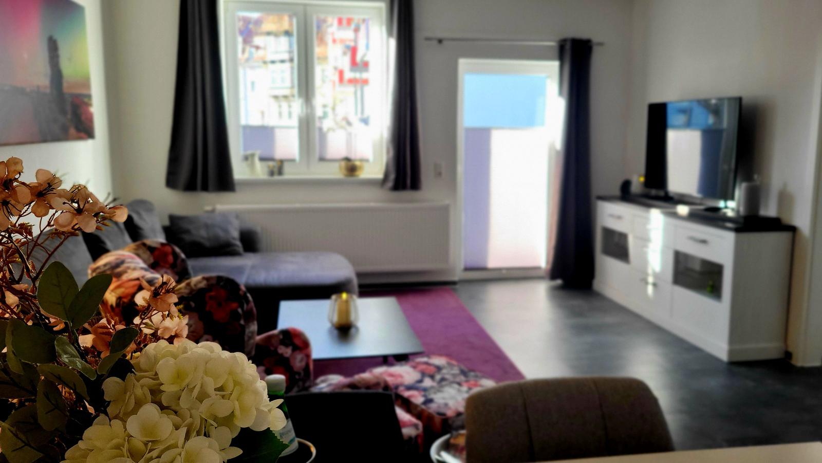 Wohnzimmer mit Sofa, Fernseher und Fenster zur Terrasse.