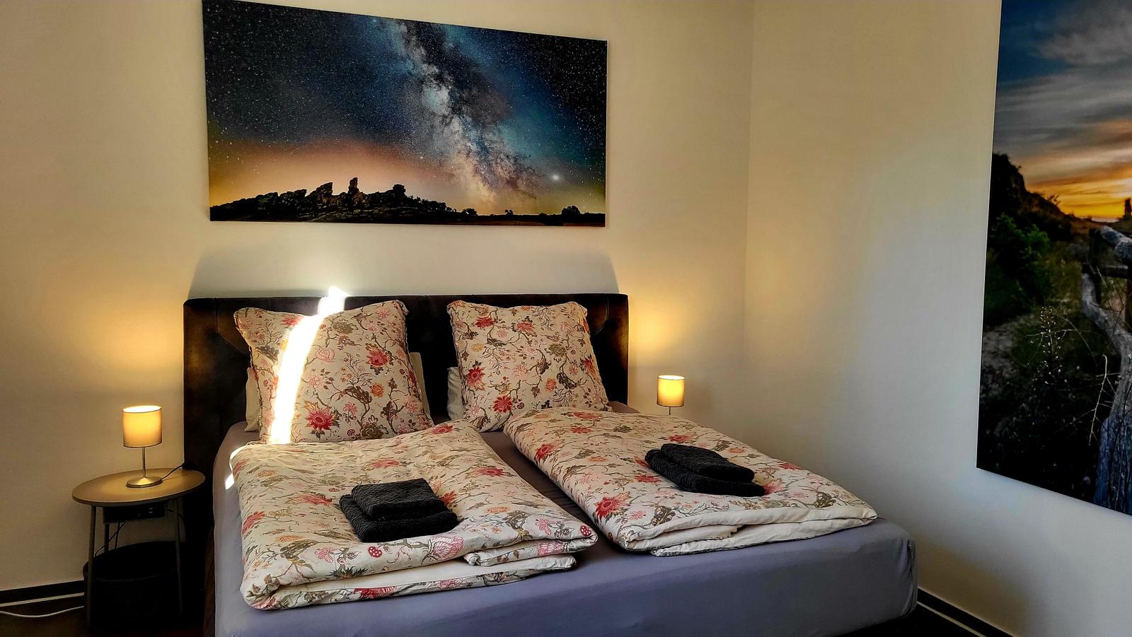 Schlafzimmer mit Bett, zwei Nachttischen und Wandbildern.