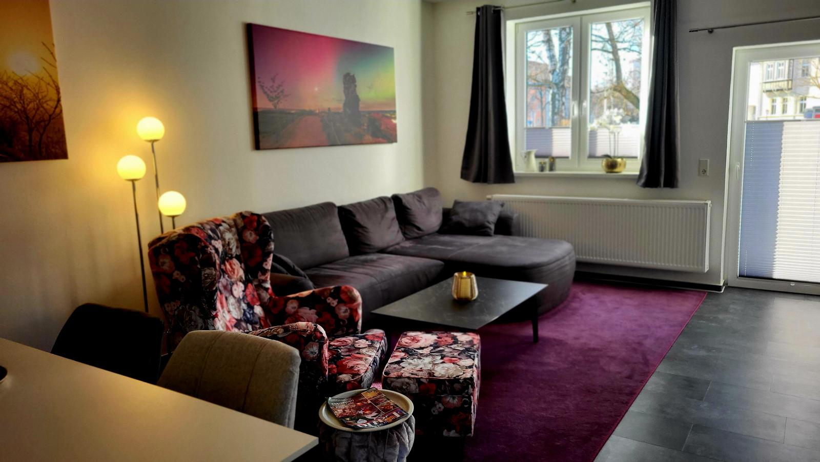 Wohnzimmer mit Sofa, Sessel und Teppich. Fenster und Tür bieten Licht.