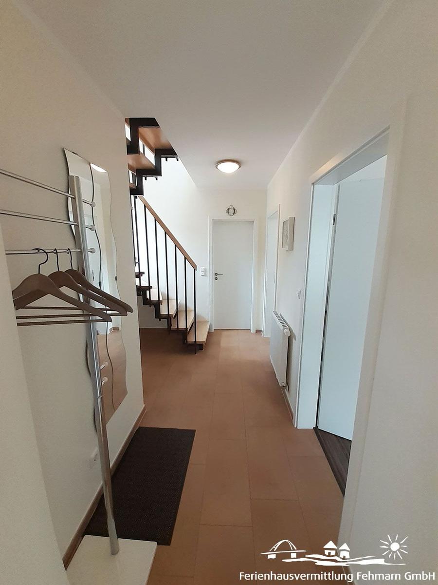 Hallway with coat rack, staircase, and doorways. Tile floor and white walls.