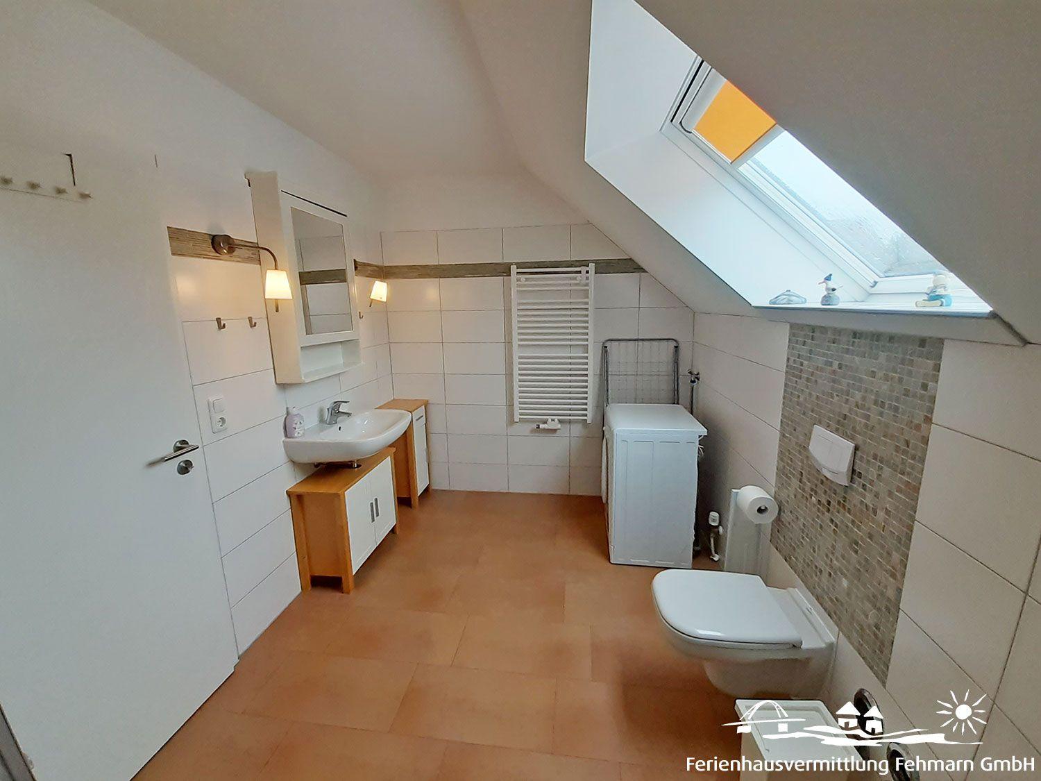 Bathroom with sloped ceiling, washing machine, toilet, and skylight.