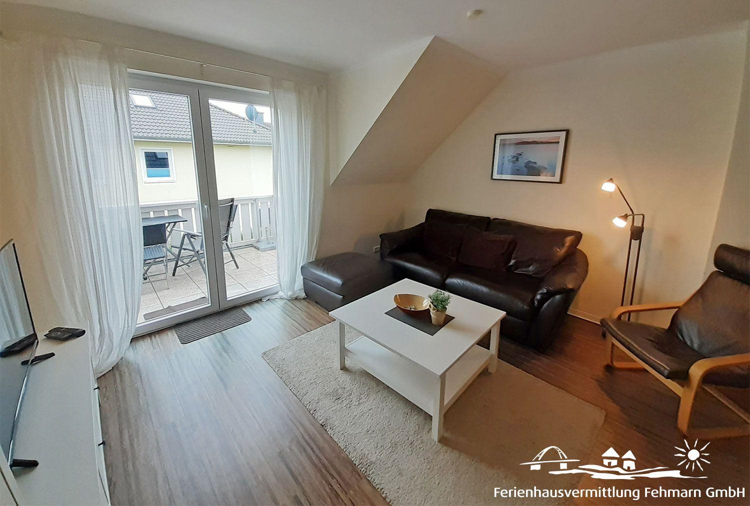 Living room with sofa, armchair, and terrace. Wooden floor and white coffee table.