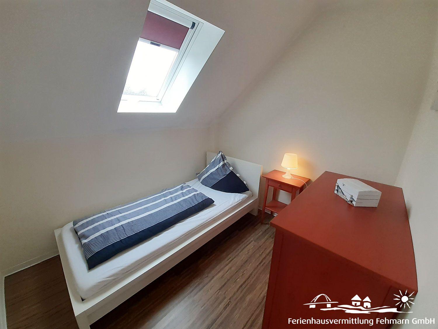 A bedroom with sloped ceilings, a bed, nightstand, and dresser.