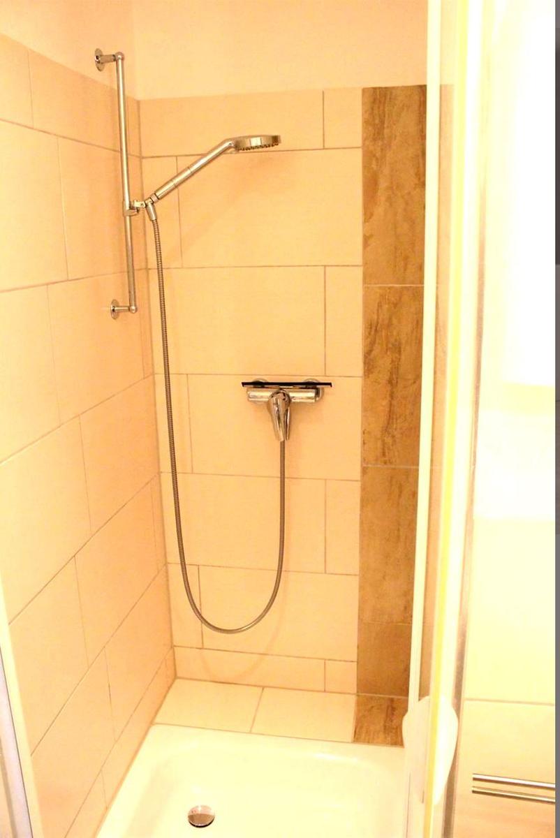 Dusche mit Duschbrause und Handbrause, Wandfliesen und Bodenfliesen.