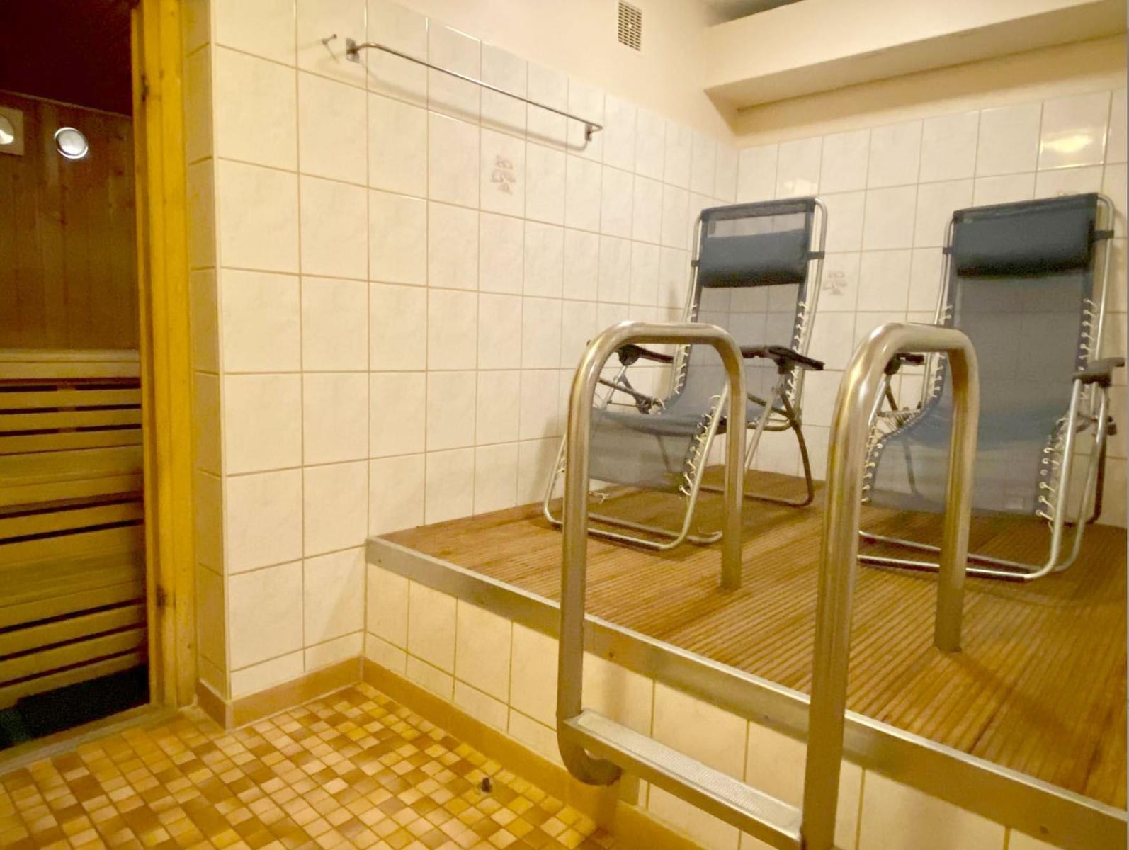 Sauna mit zwei Liegestühlen und Metallgeländern. Fliesenwand und Holzboden.