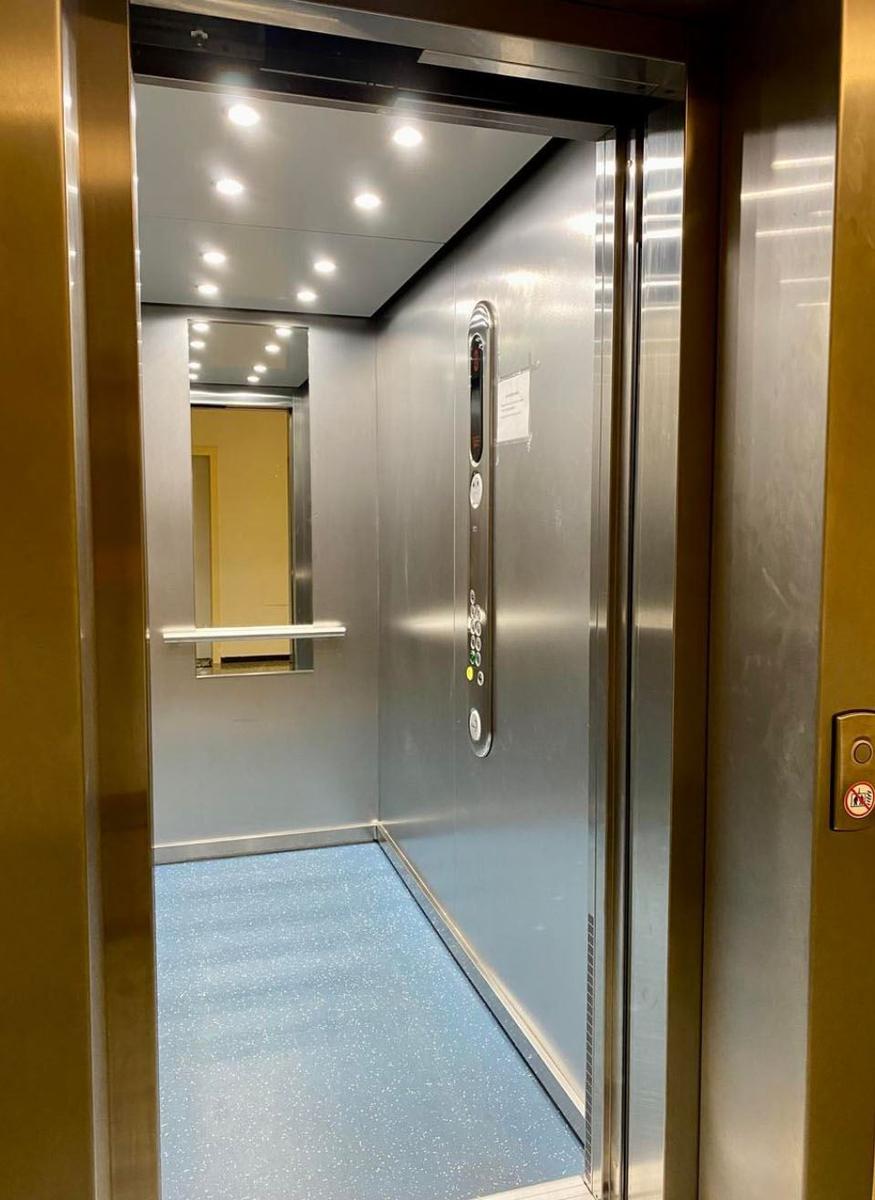 Aufnahme des Aufzugs mit metallischen Wänden und blauem Bodenbelag.