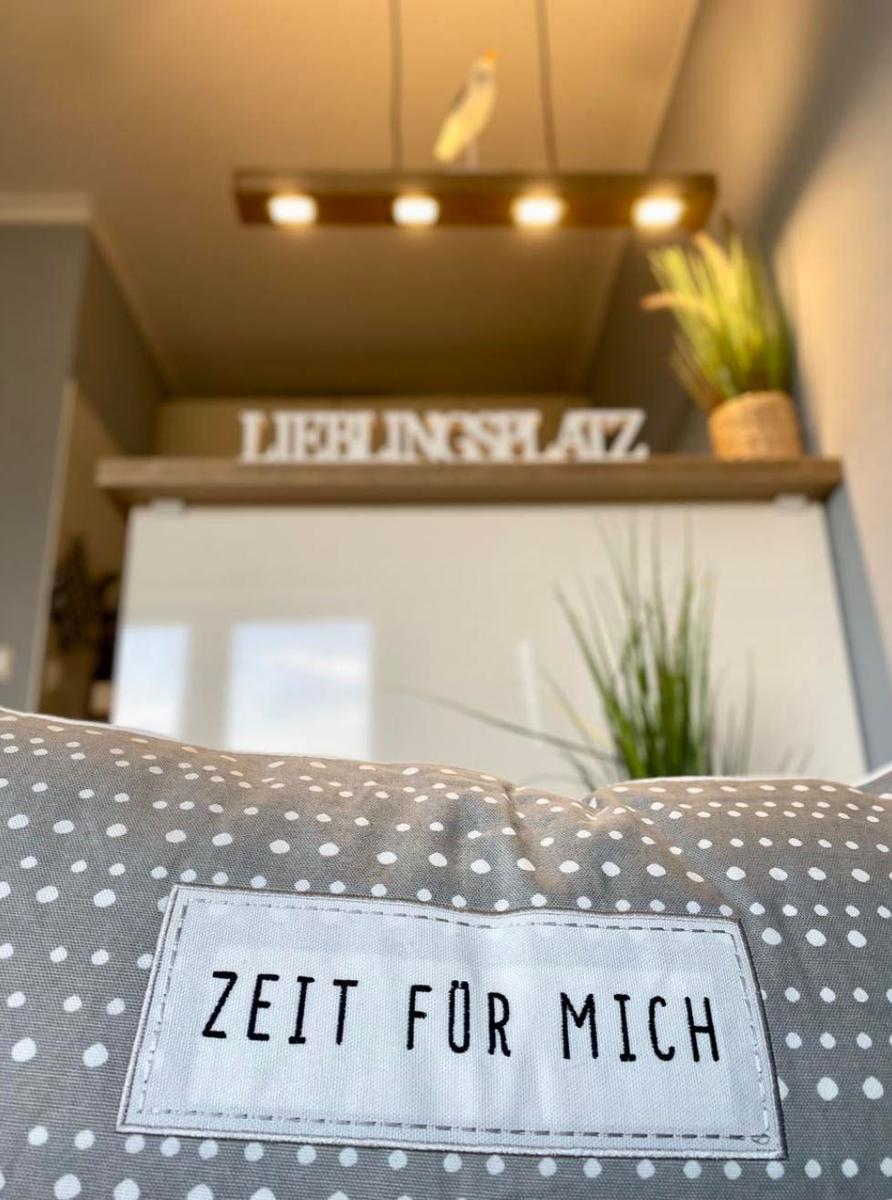 Ein Kissen mit Aufnäher steht vor einer Küchenzeile mit Schriftzug und Pflanzen.