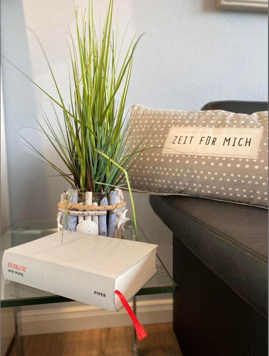Auf einem Tisch steht ein Buch, eine Pflanze und ein Kissen mit Aufschrift.