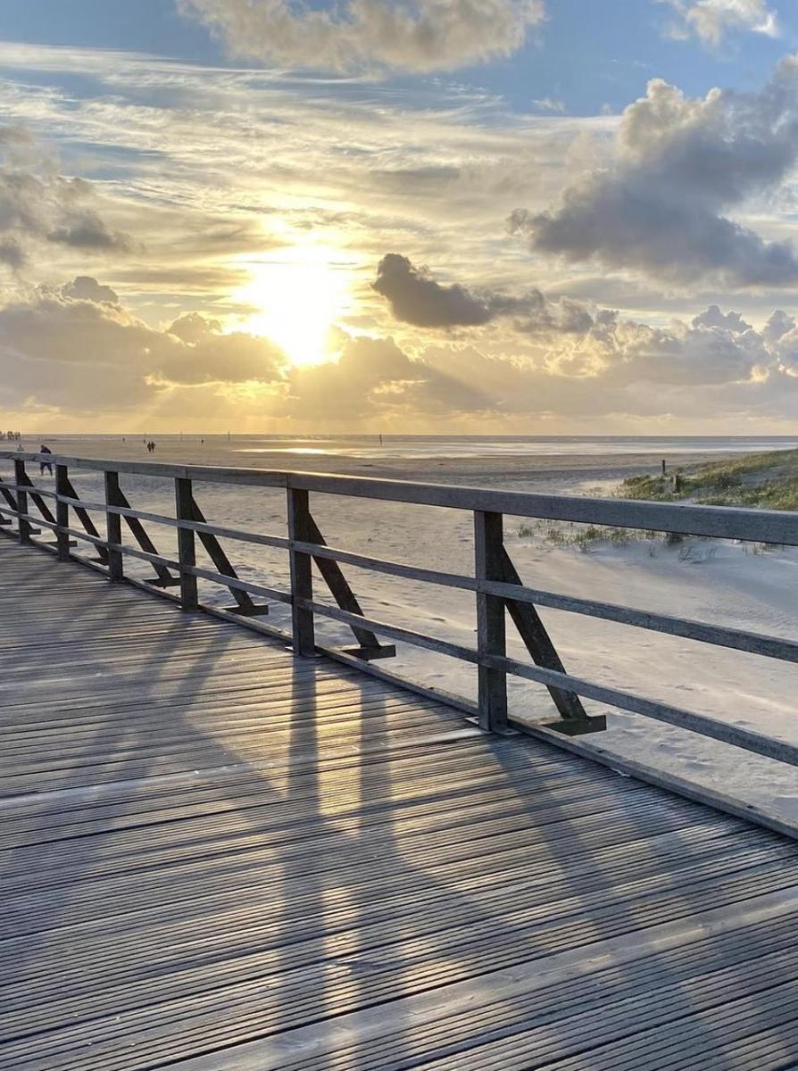 Holzpromenade führt zum Strand bei Sonnenuntergang mit dramatischen Wolken.