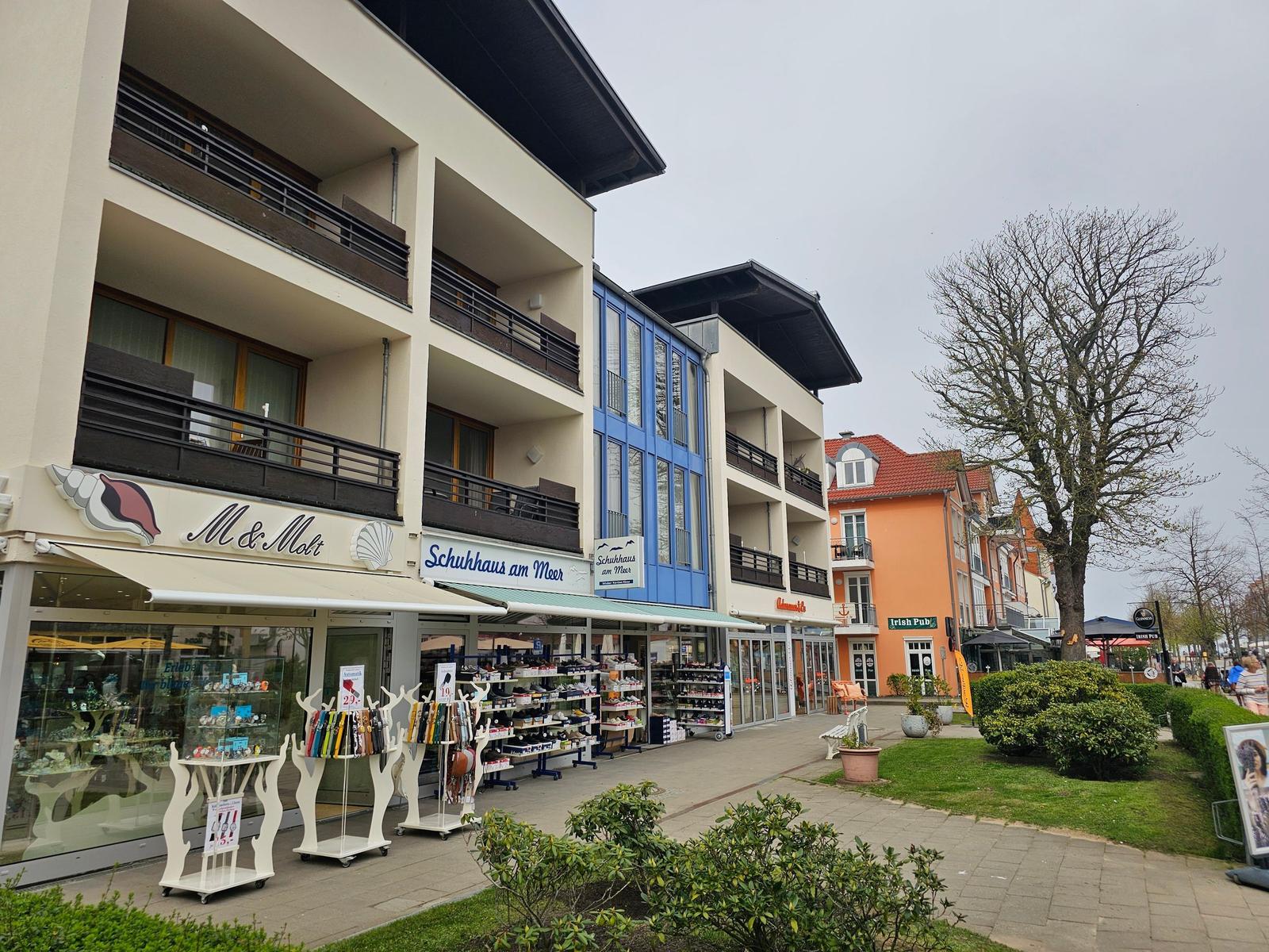 Strandnahe Geschäfte mit Schuhgeschäft und Irish Pub. Mehrstöckige Gebäude mit Balkonen.