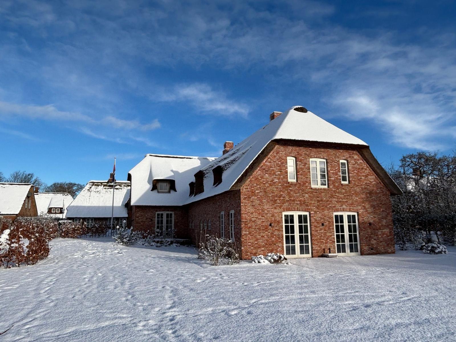 Rotes Backsteingebäude mit schneebedecktem Dach und weißen Fenstern.
