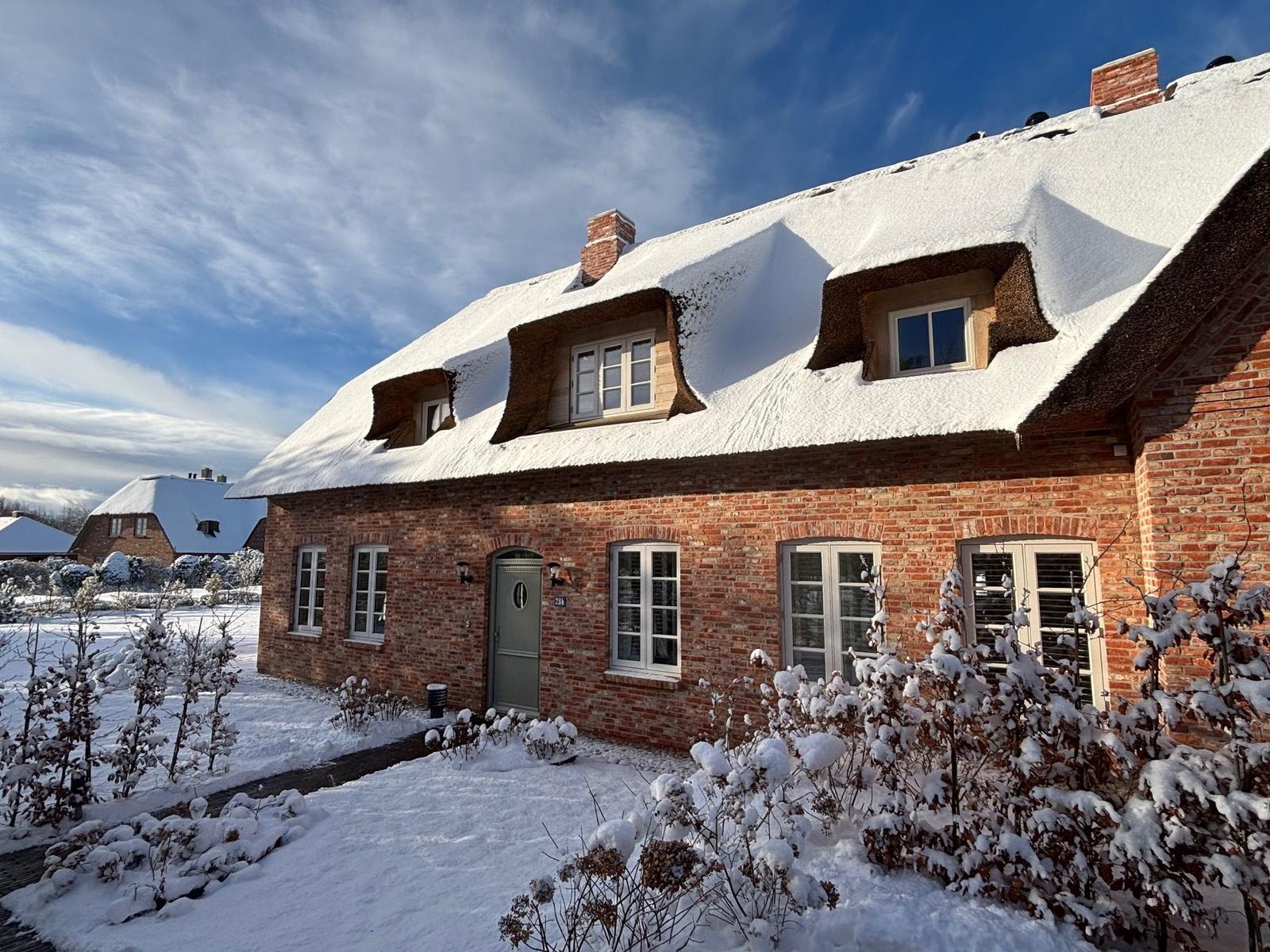 Rotes Backsteingebäude mit schneebedecktem Dach und Fenstern.