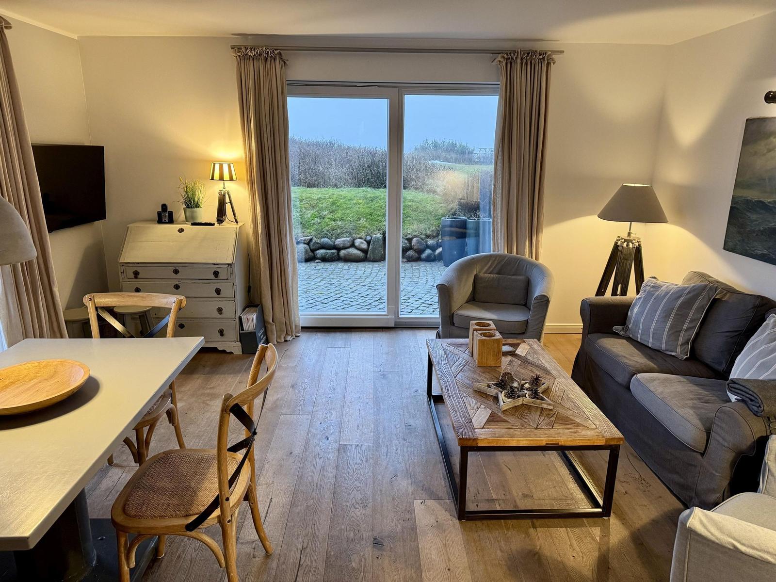 Wohnzimmer mit Sofa, Sessel und Essbereich. Durchgang zur Terrasse mit Blick auf Grasland.
