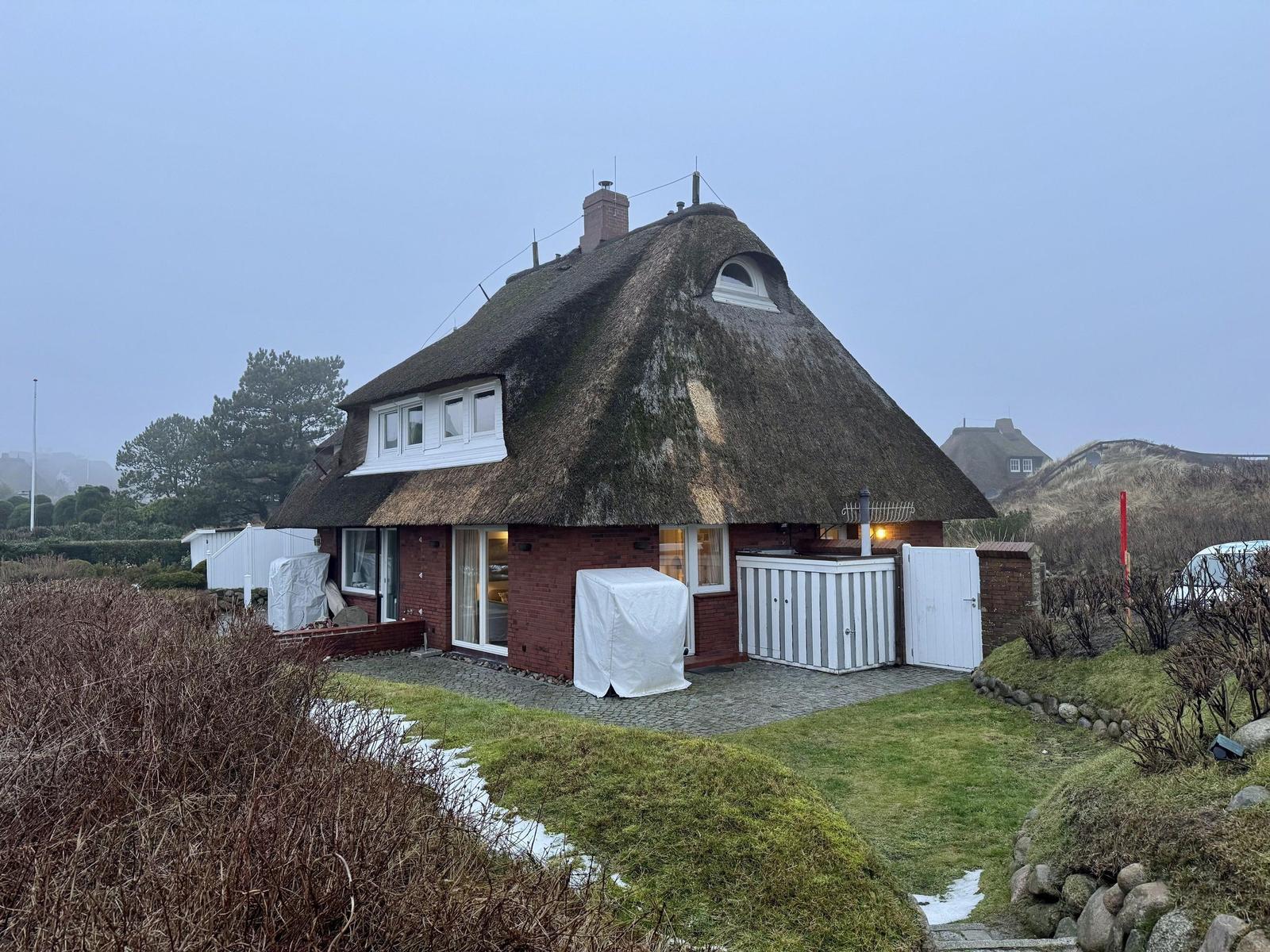 Rotes Haus mit Strohdach, weißer Toranlage und Garten.