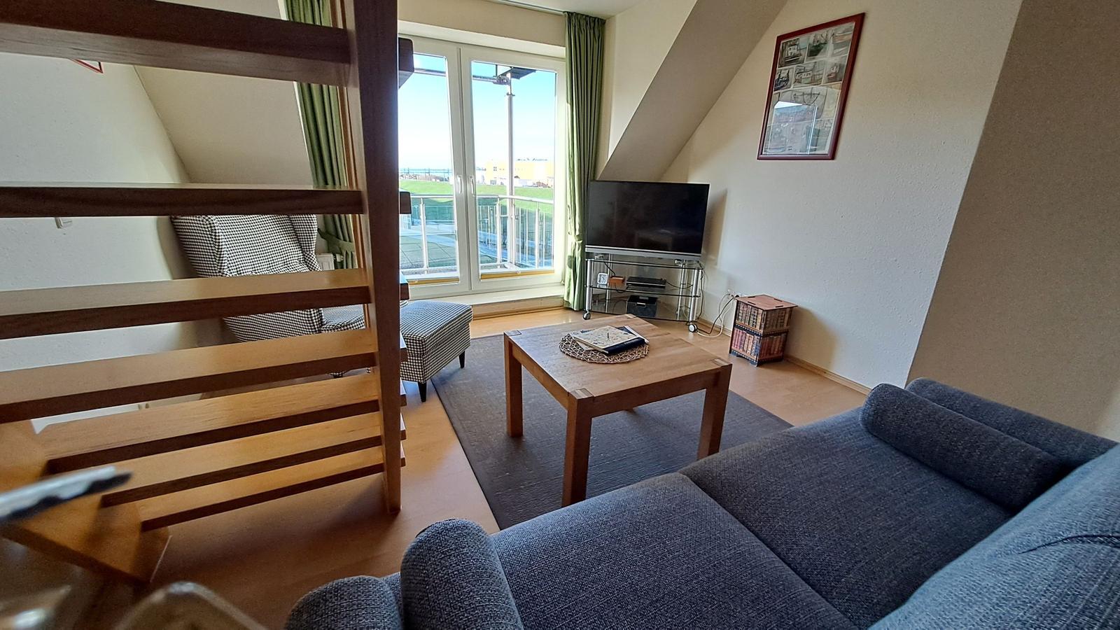 Wohnzimmer mit Sofa, Couchtisch und TV. Balkon mit Blick auf Grünflächen.