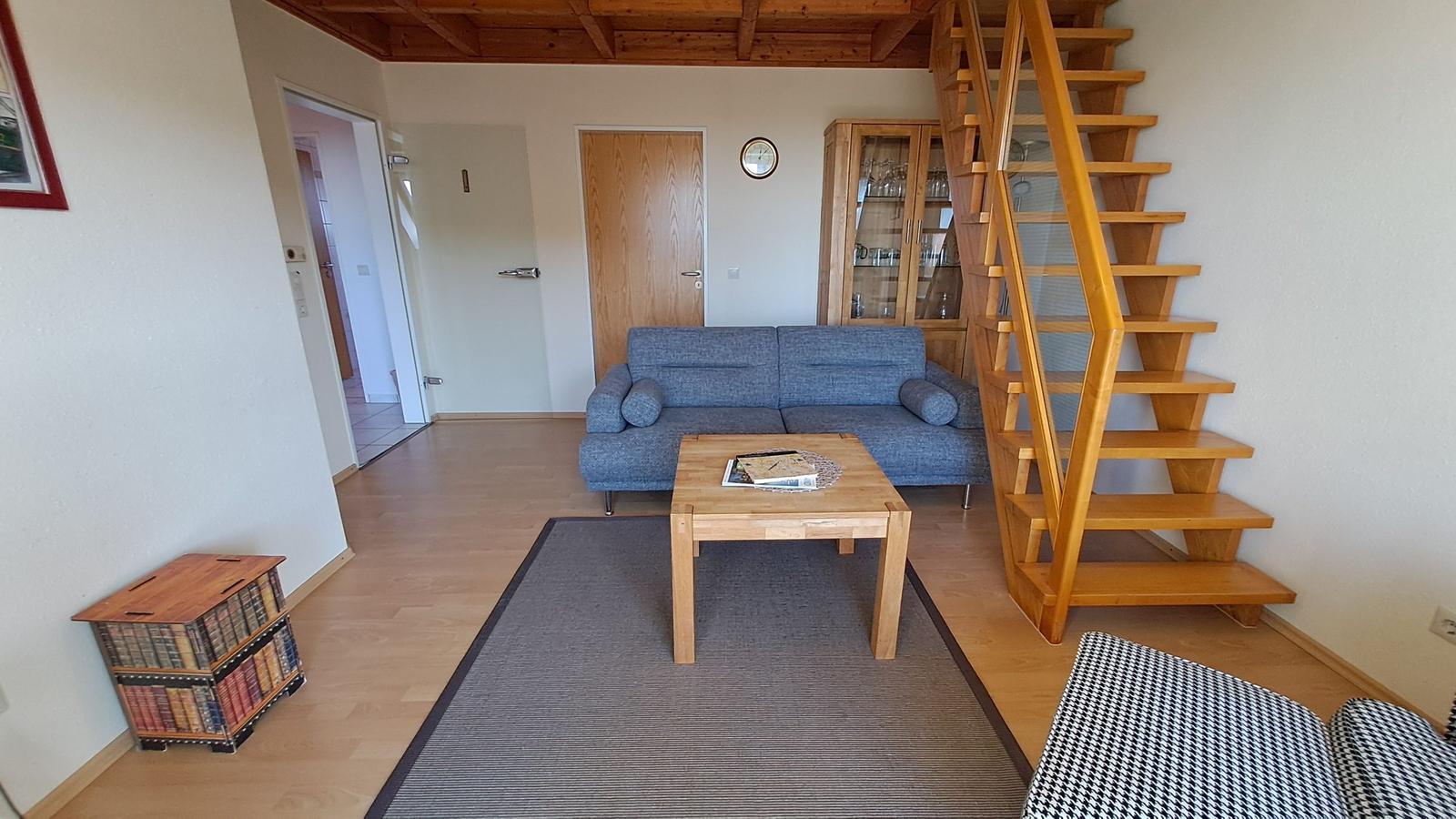 Wohnzimmer mit Sofa, Tisch und Holztreppe.