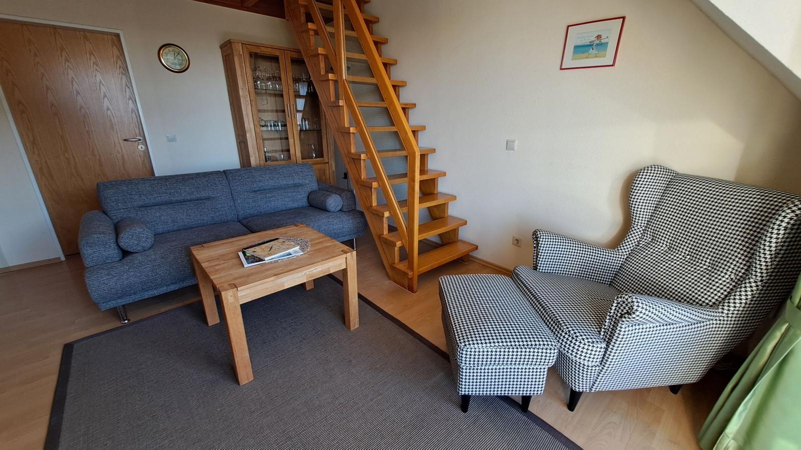 Wohnzimmer mit Sofa, Sessel und Holztreppe