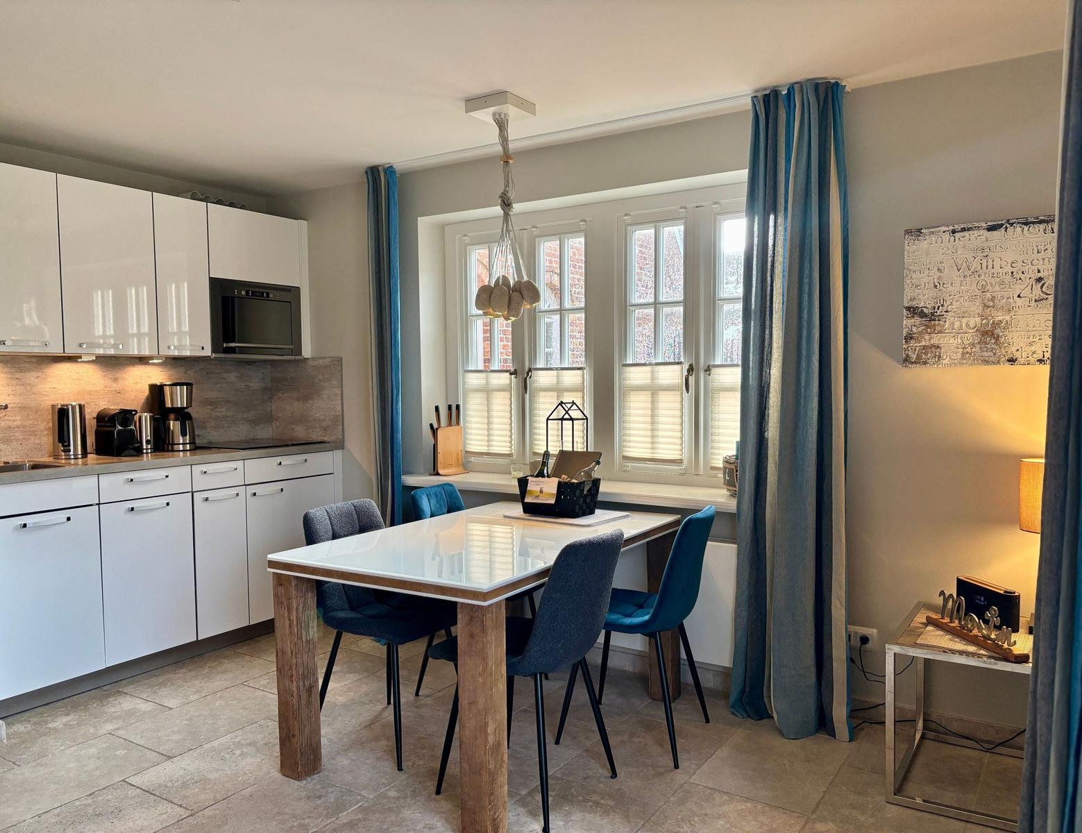 Kitchen with dining table, windows, and curtains. Living area with table and lamps.