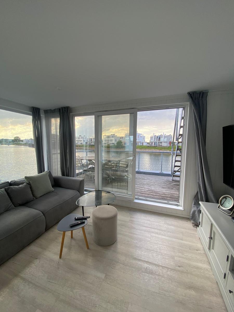 Living room with view of water and terrace with table and chairs.