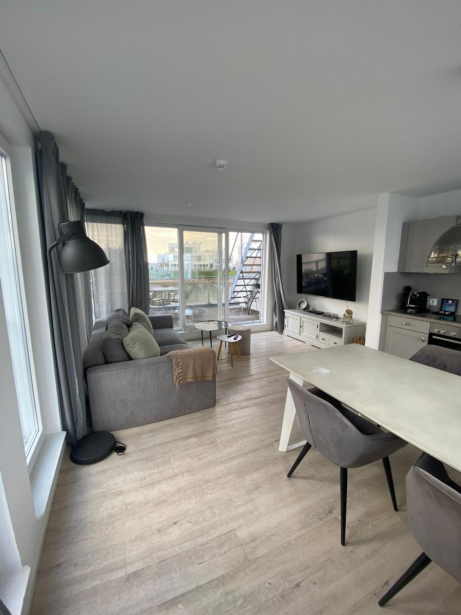 Living and dining area with sofa, TV, and view of balcony.